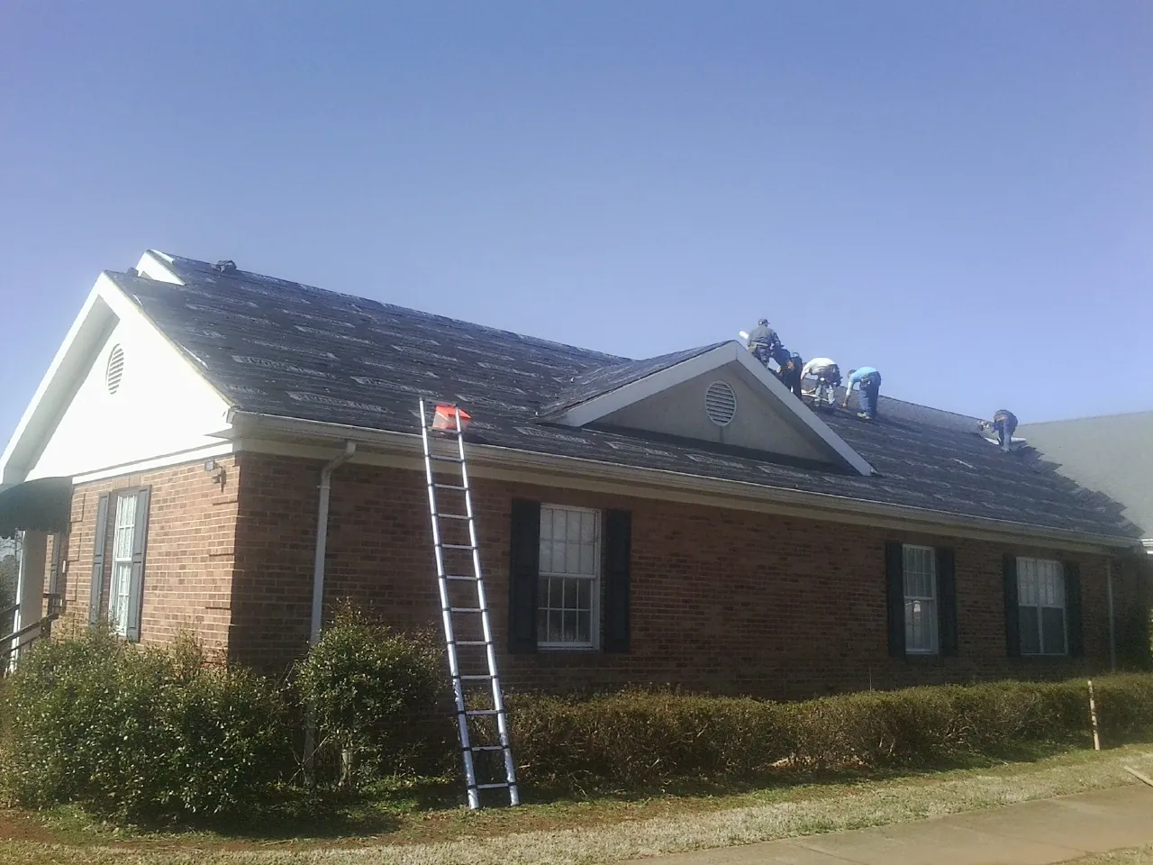 Crew tearing shingles off a brick ranch roof with a ladder set — Metal Roof Repair work by our crew in Viola