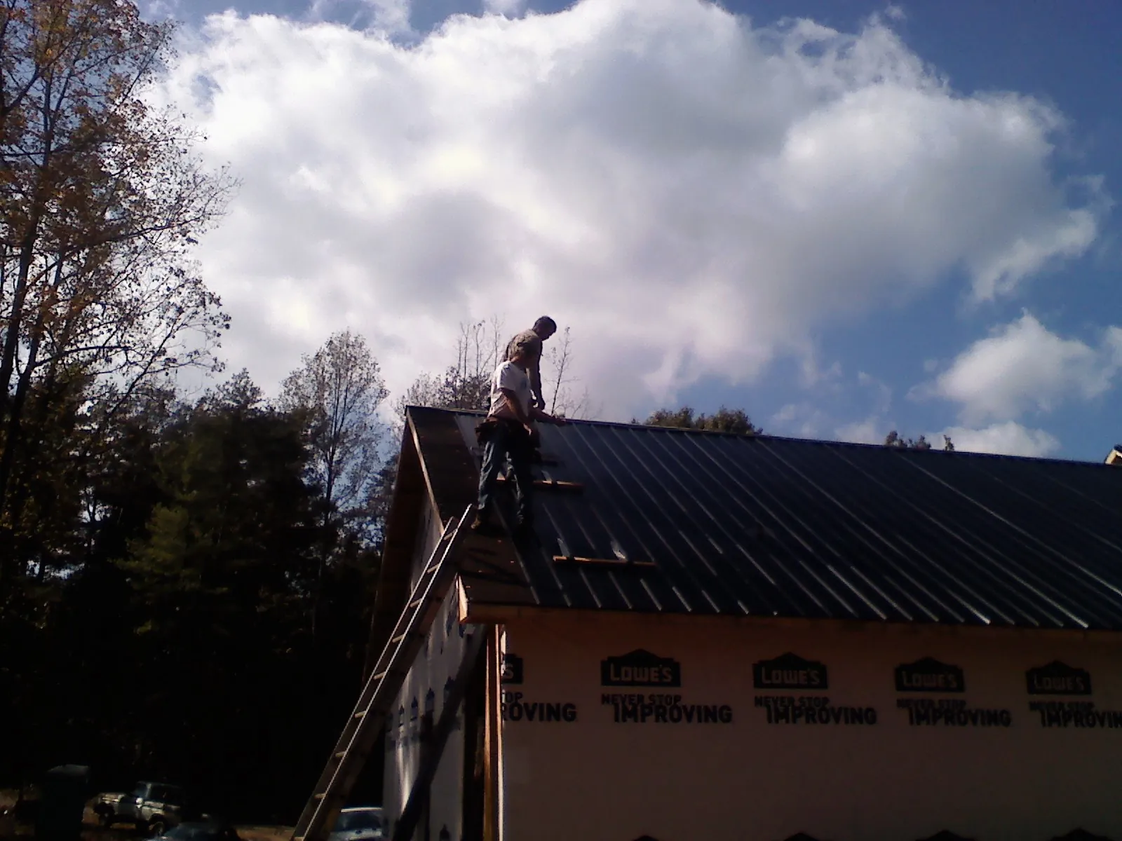 Roofer fastening dark metal panels high against a cloudy sky, from a Roof Inspection job in Viola